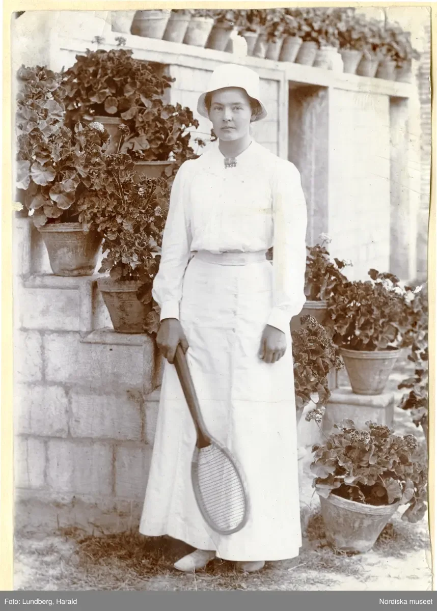 Porträtt av Marie-Louise Flygare (g. Lundberg) i Persien 191314. Hon är klädd i ljus klännning och solhatt och håller i ett tennisrack. — تصویر رکورد یوروپیانا