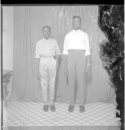 Two young men wearing shirts and pants, each with a cigarette in his mouth and a watch on his wrist, both standing face-forward in the studio. — تصویر رکورد یوروپیانا