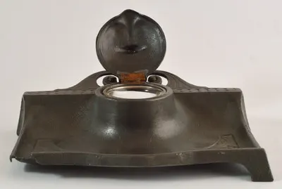 Călimară de birou de formă dreptunghiulară realizată din metal. Se sprijinea pe patru picioare, lipsește unul. În partea centrală se găsește rezervorul de formă cilindrică pentru cerneală, realizat di — تصویر رکورد یوروپیانا