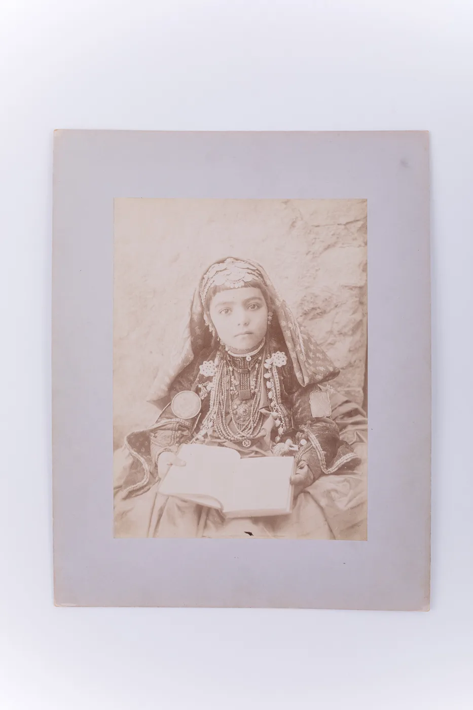 Fotografie de exterior ce prezintă o fetiță în costum foarte elaborat (evreiesc sau din tribul Shasvan, din estul Iranului). Aceasta ține în mâini o carte. Se remarcă bujuteriile purtate de copil. Ima — تصویر رکورد یوروپیانا