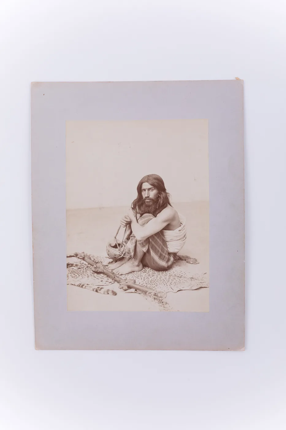Fotografie de atelier ce prezintă un bărbat dervish. Acesta este așezat pe o blană de tigru, în mână ține un vas pentru cerșit, iar în fața sa se află un toiag. Imaginea este realizată pe hârtie album — تصویر رکورد یوروپیانا